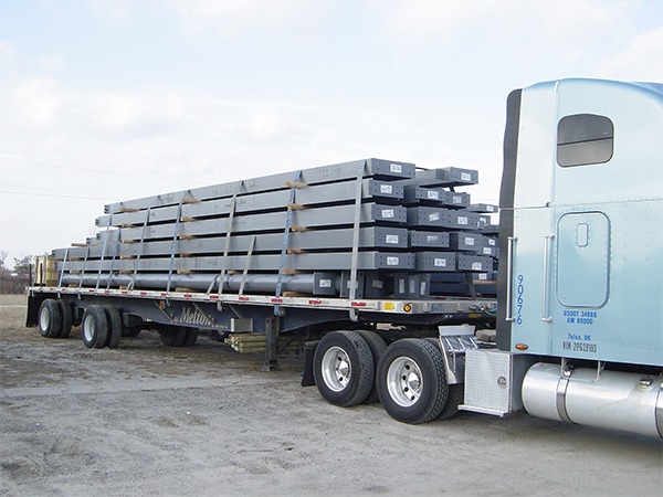 Flatbed truck transporting stacked pre-engineered steel beams to construction site.